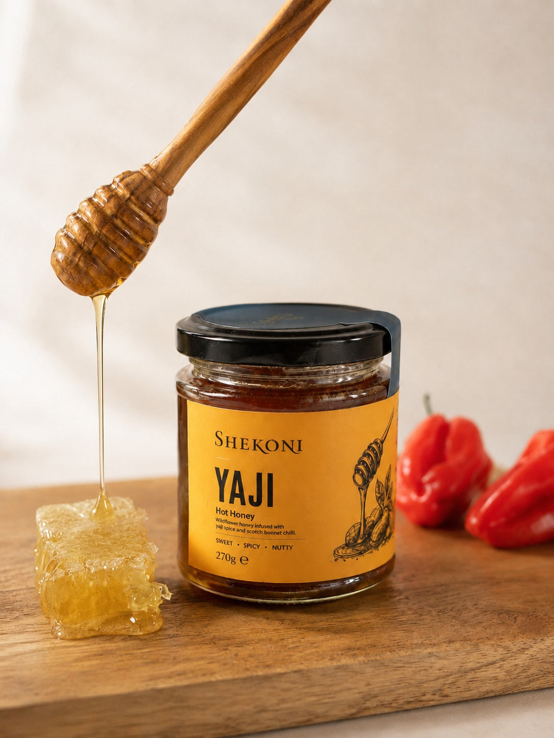 Yaji hot honey pouring from a dipper beside honeycomb and scotch bonnet chillies