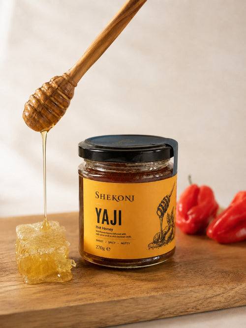 Yaji hot honey pouring from a dipper beside honeycomb and scotch bonnet chillies